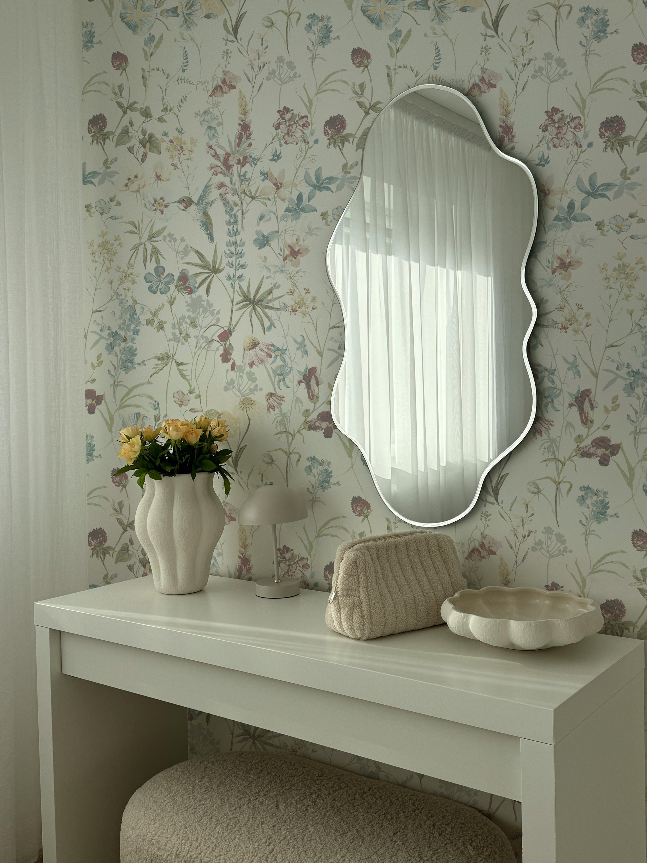 A stylish dressing area adorned with the Soft Feathered Blooms Wallpaper, featuring gentle floral prints and fluttering birds. The soft colors and natural elements provide a tranquil backdrop, complemented by a contemporary mirror and minimalist decor.