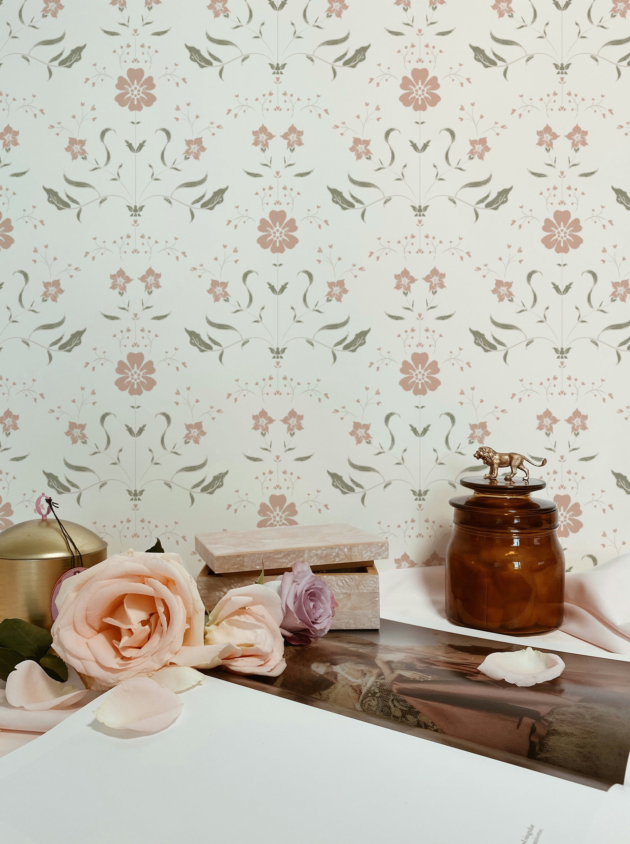 Elegant workspace setting featuring a vintage-style floral wallpaper with soft pink and green designs. The scene is decorated with fresh roses, a decorative box, and a vintage amber glass jar with a small elephant figurine on top, creating a charming and inviting atmosphere.