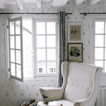 A serene reading nook with a large, plush armchair positioned near a bright window, surrounded by walls adorned with snow pea wallpaper. The scene exudes a calm, inviting atmosphere enhanced by natural light and minimalist decor.