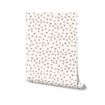 A roll of Simple Meadow Wallpaper, featuring a light design of small, spaced-out flowers with black centers and peach petals on a white base, ready to be applied for a subtle and elegant room transformation