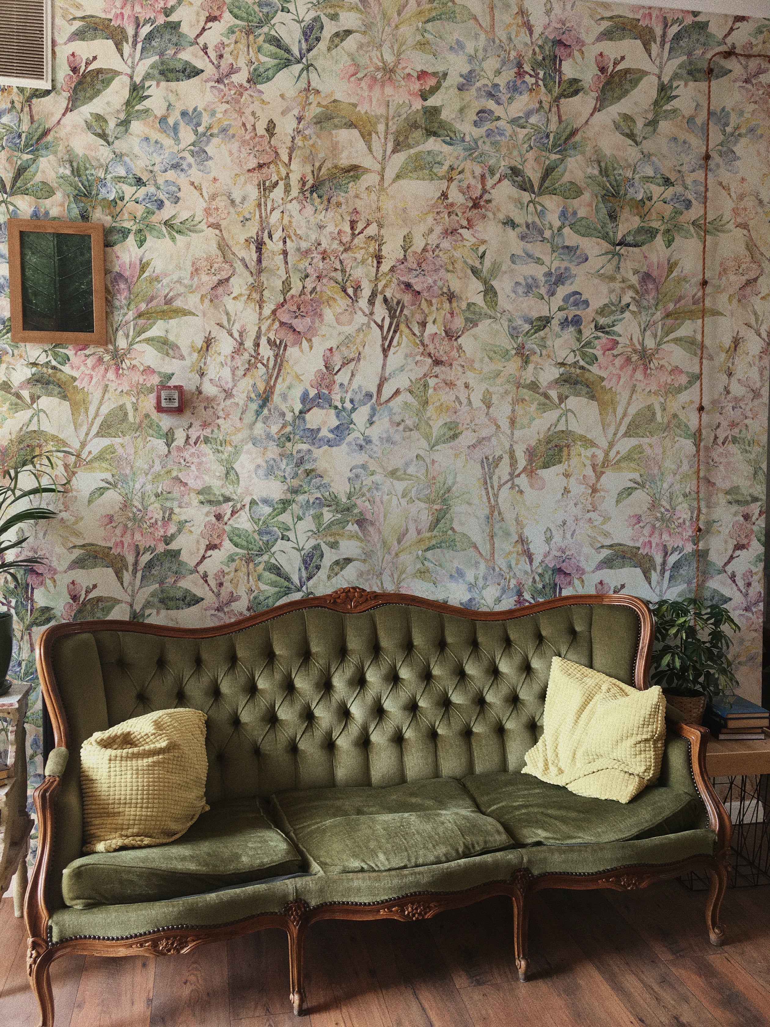 A stylish interior showcasing the "Ancient Florals Wallpaper," creating a rich, textural backdrop for a vintage green tufted sofa adorned with yellow cushions. The room's ambiance reflects a harmonious blend of classic and contemporary styles, highlighted by the intricate floral patterns.