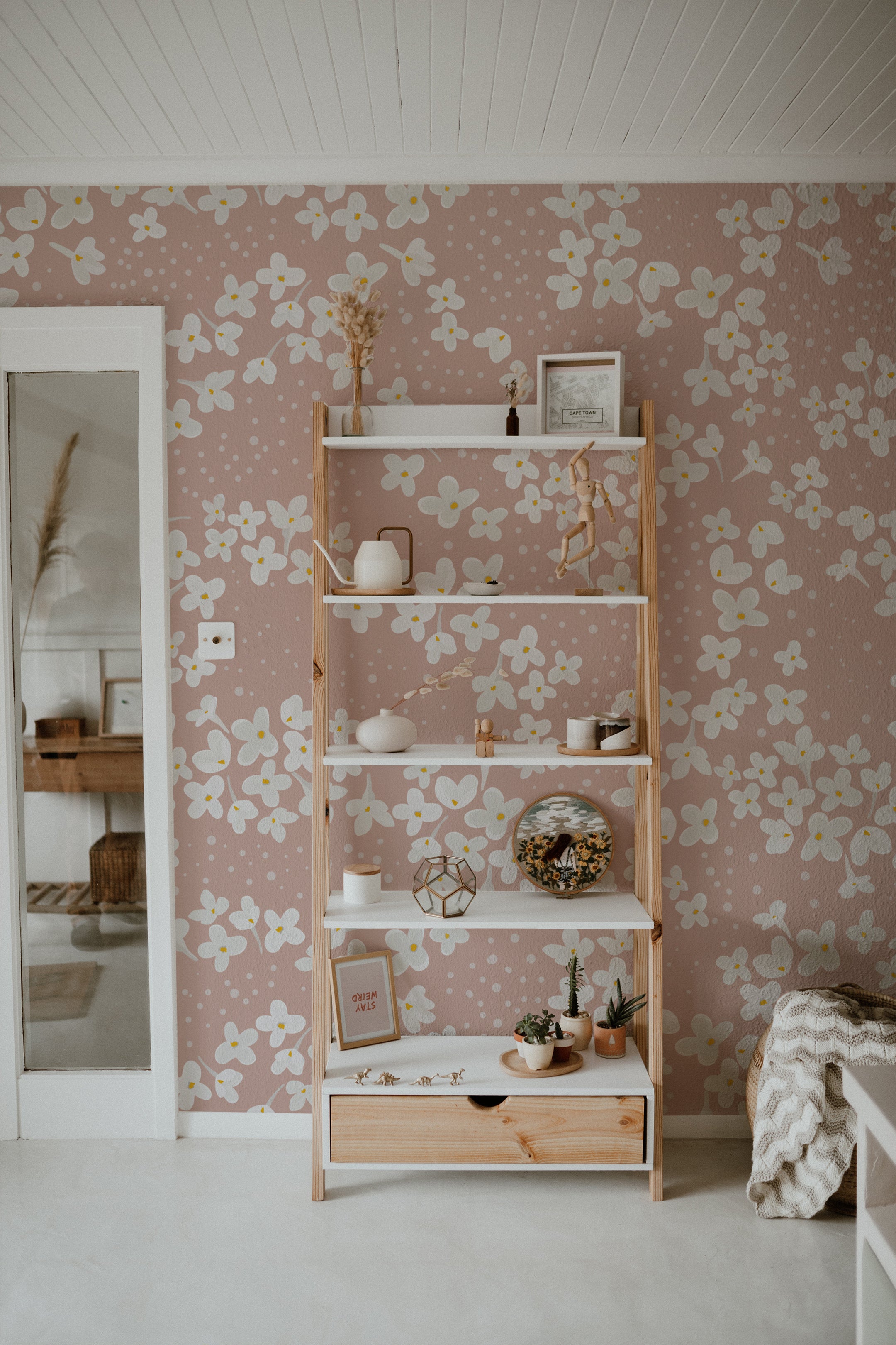 A stylish shelving unit against the Fleur de Printemps Wallpaper in a living room, showing off the wallpaper’s large floral patterns and dotted texture that enhances the room's aesthetic.