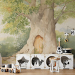 A playful children's area with a mural of a large tree with a door, styled after Winnie the Pooh's house, flanked by children’s storage units and toys, under a leafy green canopy.