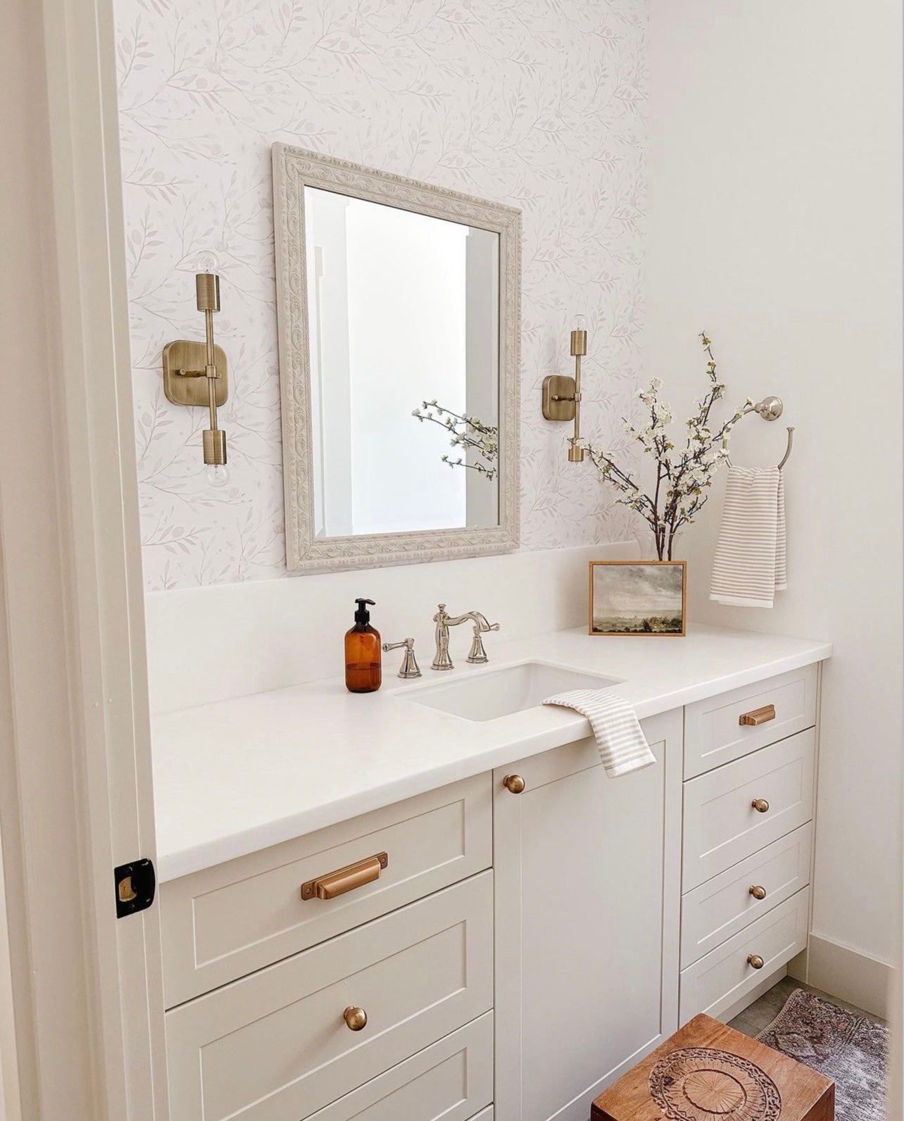 An elegant bathroom vanity with brass fixtures and framed mirror, complemented by the 'Spring Bird' wallpaper’s subtle, nature-inspired design