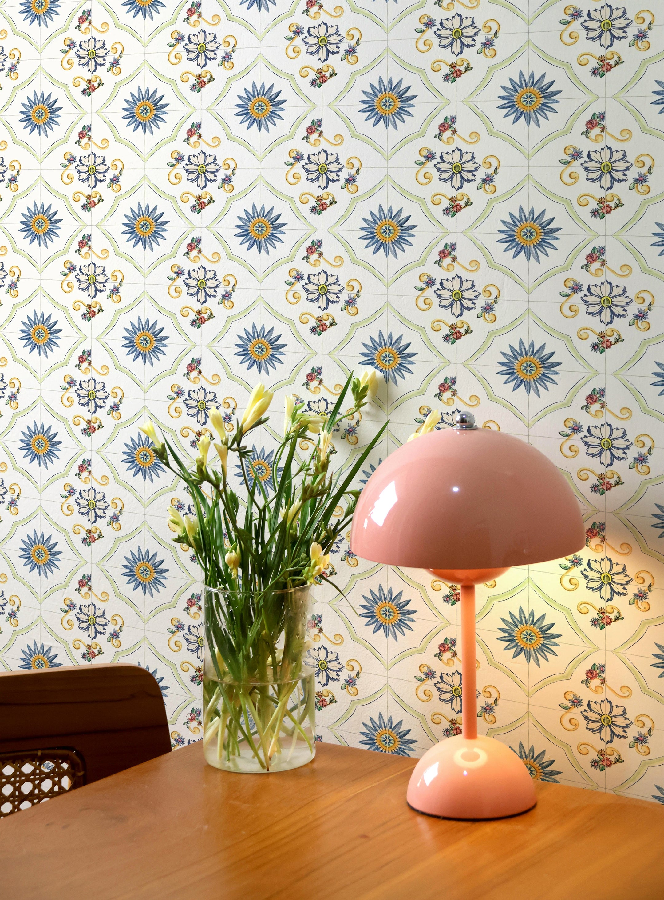 An interior setting with the Spanish Tile Wallpaper in the background enhancing a mid-century modern decor. A pastel pink mushroom lamp sits on a wooden table, alongside a vase with fresh tulips, creating a warm and inviting ambiance