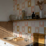 Warm and inviting kitchen scene with Coralie Wallpaper featuring large squares in shades of peach, beige, and gold, each with a decorative sunburst center. The wallpaper complements the wooden countertops and white cabinetry, creating a cozy atmosphere.