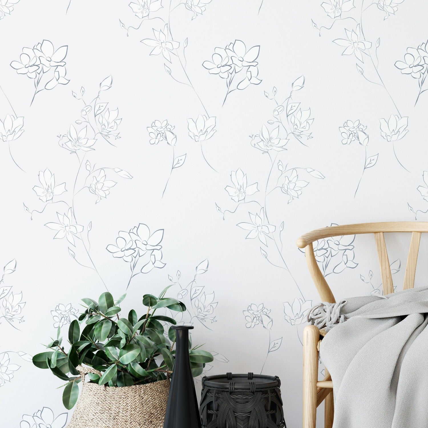 A styled room corner featuring the Minimal Floral Wallpaper IX as a backdrop, enhancing the space with its understated floral outlines. A woven basket with lush green plants and a wooden chair with a cozy blanket highlight the wallpaper's serene and clean design.