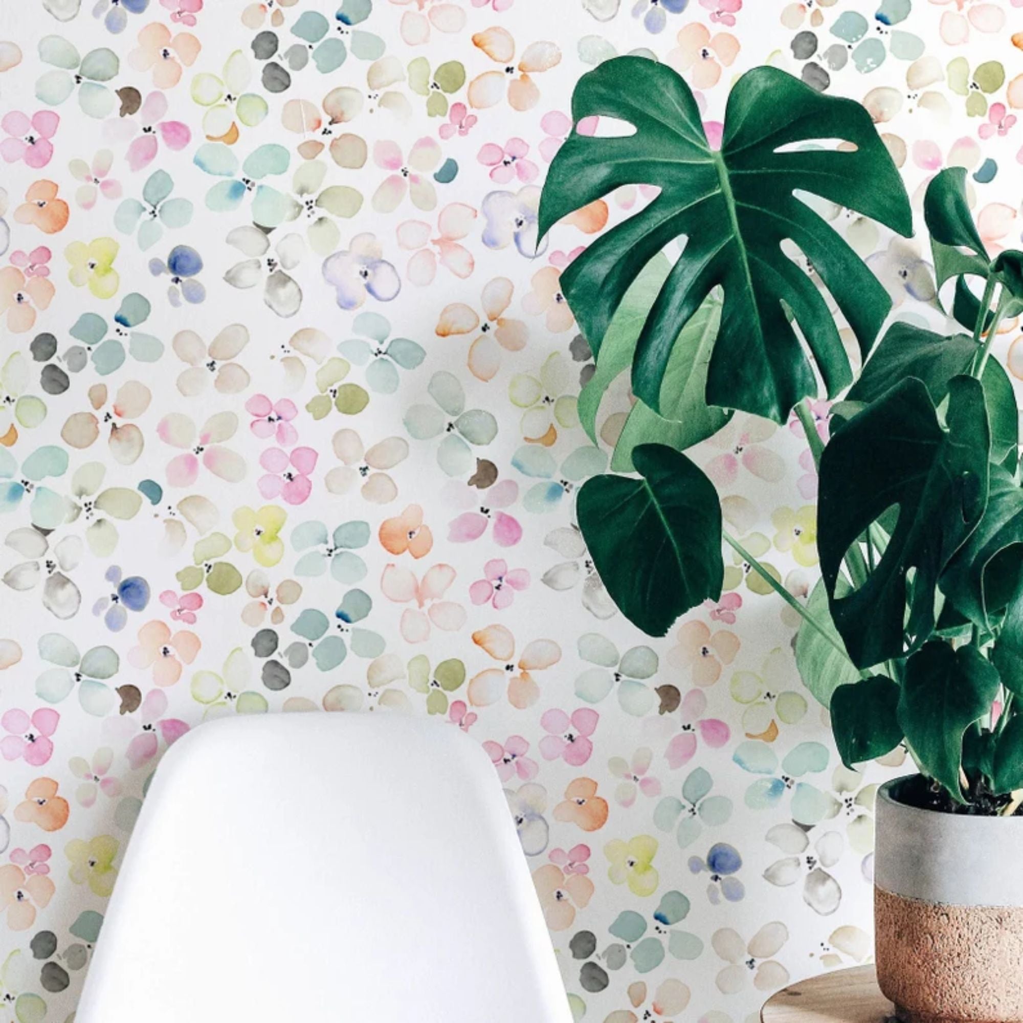 A contemporary corner of a room is brightened by the Hand Painted Floral Wallpaper, accompanied by a lush monstera plant and a sleek white chair. The wallpaper's lively colors and patterns contribute to a dynamic yet peaceful environment.