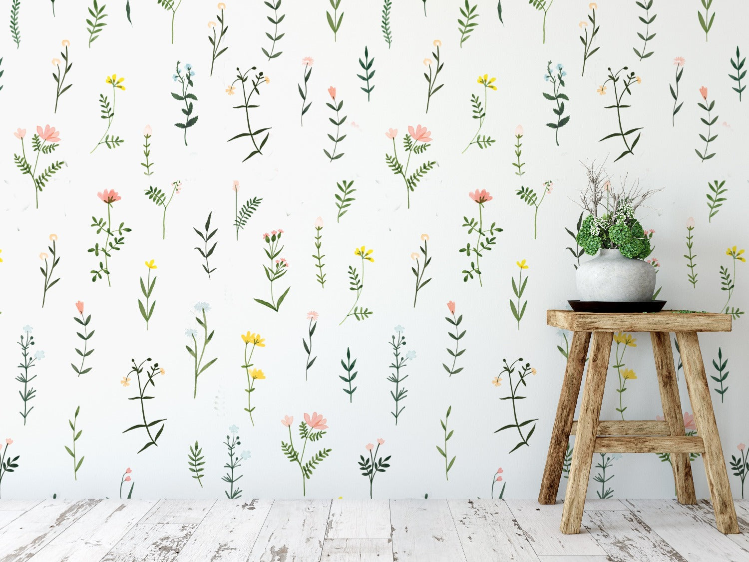 A rustic wooden stool stands against a wall adorned with 'Floral Wallpaper - XII'. The wallpaper's cheerful botanical pattern featuring small, sprightly flowers and leaves infuses the space with a light, airy ambiance, reminiscent of a spring day in the countryside.