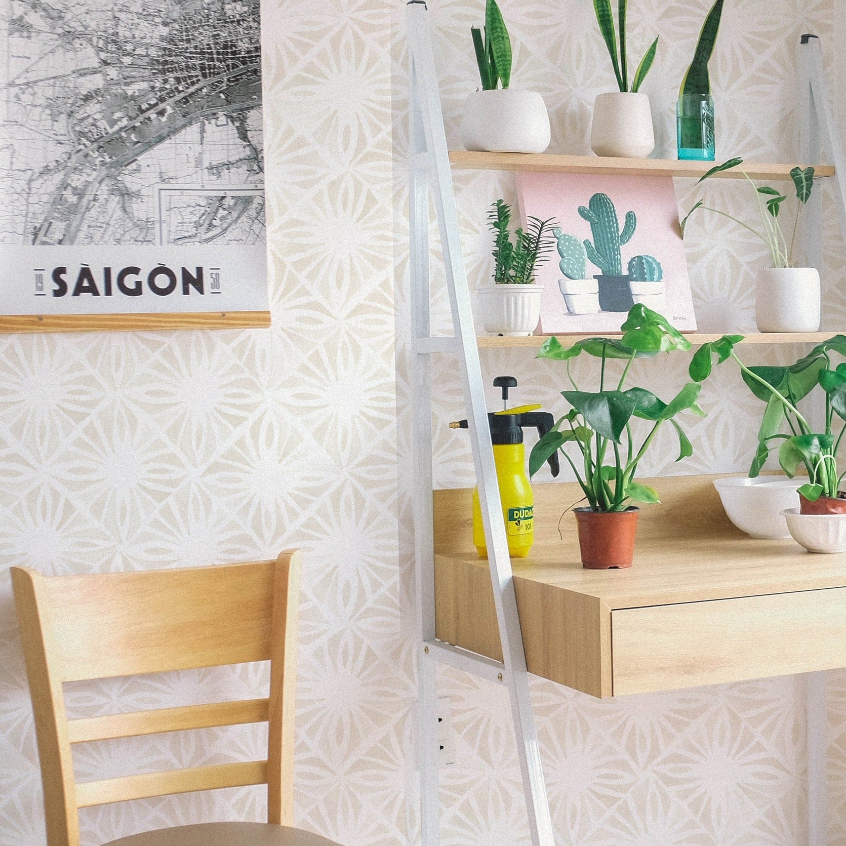 A bright, airy corner of a room is accented by the Moroccan Tile Wallpaper II - Ecru, featuring a geometric design that gives a modern twist to traditional Moroccan tiles. The neutral wallpaper tones are paired with houseplants and a wooden workspace, creating a calm and inviting area for relaxation or creativity.