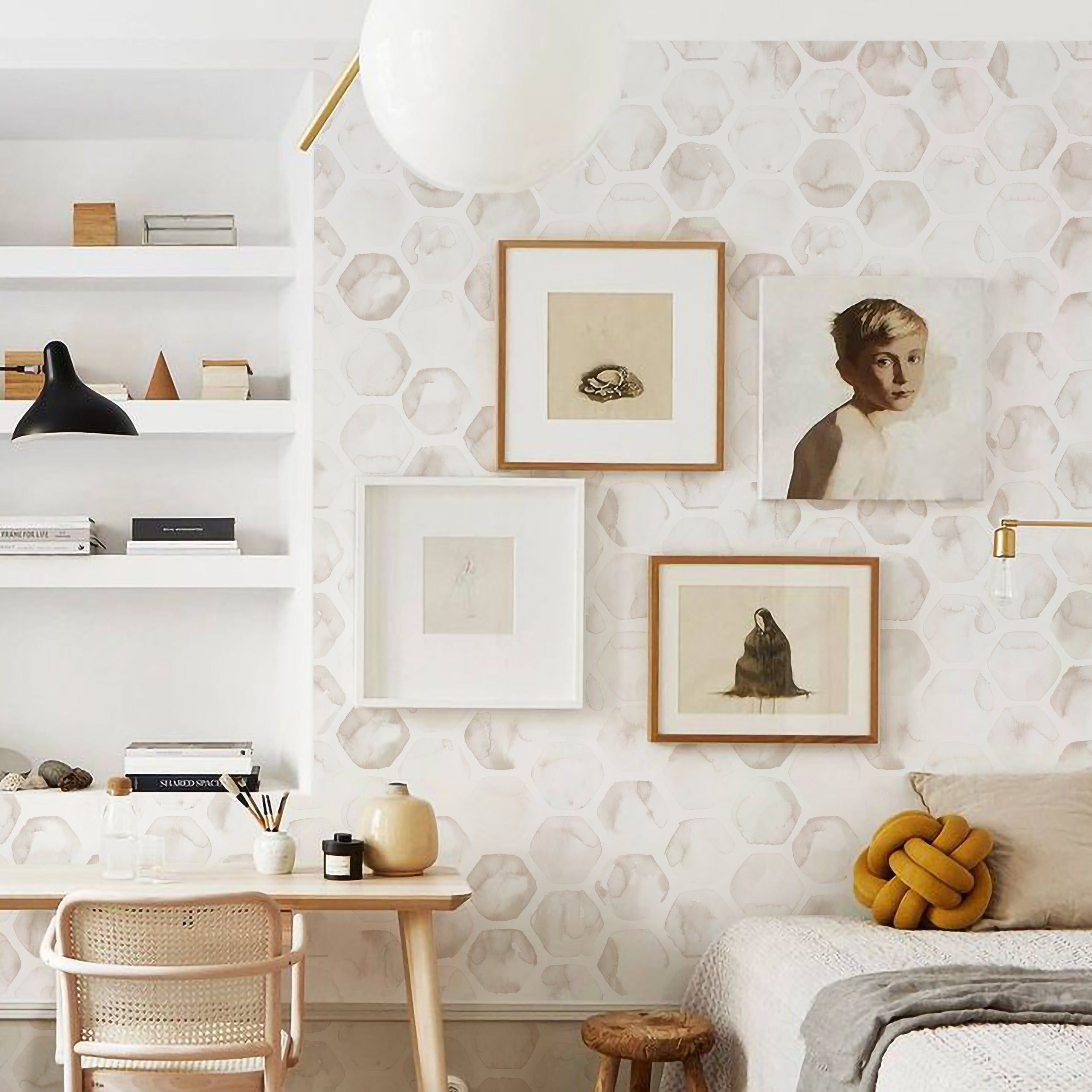 An interior design setting showcasing a wall adorned with the Watercolour Honeycomb Wallpaper, complemented by a modern minimalist décor including a white bookshelf, a wooden desk with a chair, artwork frames, and cozy textiles."