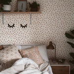 A warmly decorated corner of a bedroom with the Simple Meadow Wallpaper. This setup includes a shelf with decorative items, cozy pillows on the bed, and a small nightstand with a lamp, all complemented by the floral backdrop.