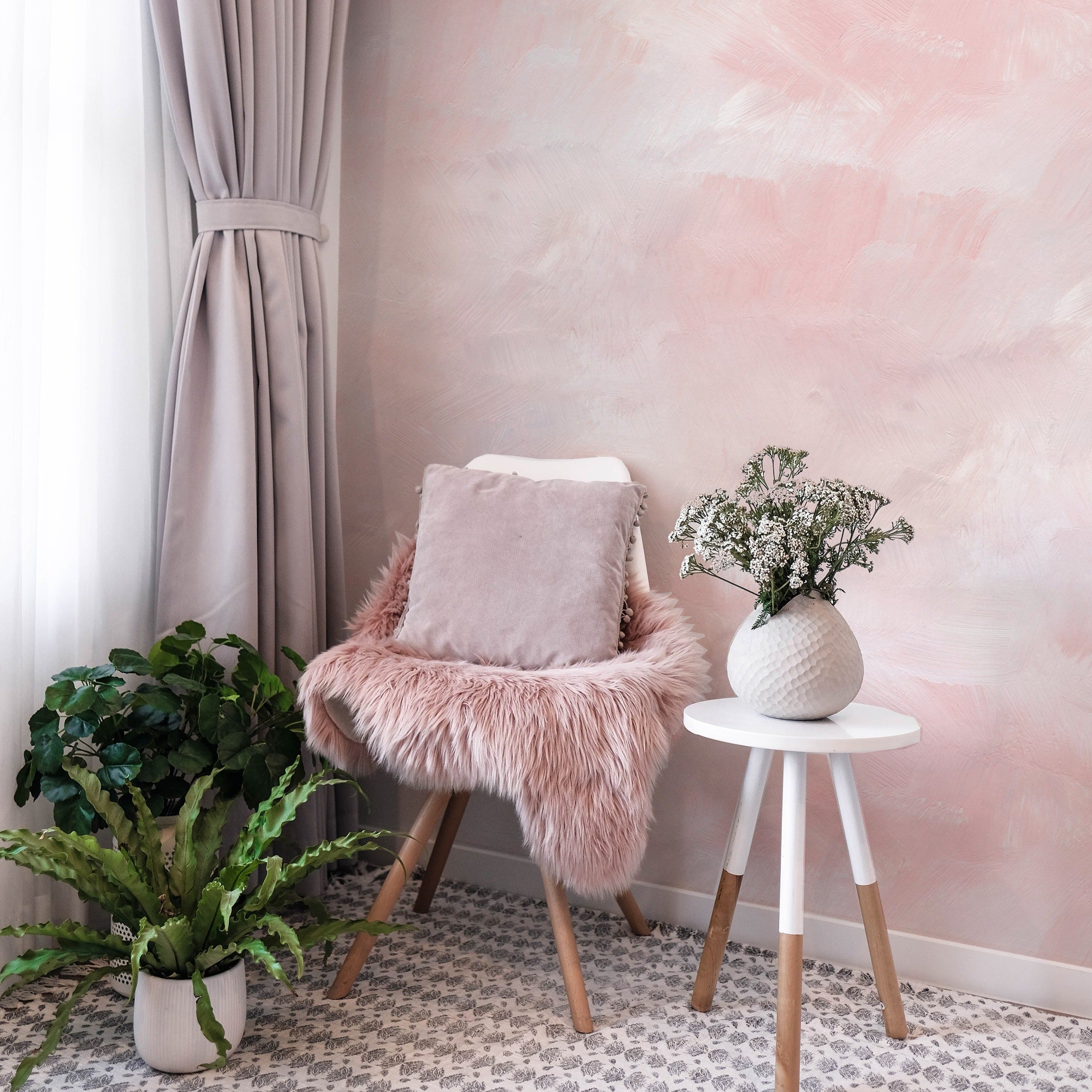 A cozy corner featuring the Venetian Watercolor Wallpaper. The space is styled with a plush chair with a furry throw, a white side table, and lush green plants, evoking a tranquil, modern vibe.