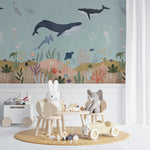 Child-friendly nursery featuring the Deep Sea Wallpaper Mural depicting a serene underwater scene with whales, dolphins, and a rich seabed of coral and marine plants, complemented by soft, child-safe furniture and toys