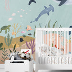Nursery room decorated with Deep Sea Wallpaper Mural showcasing an enchanting underwater scene with whales, jellyfish, and varied sea flora, alongside a white crib and playful children's toys