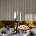 Festive dining setting against a backdrop of Classic Striped Wallpaper in beige. The table is set with elegant glassware, candles, and a holiday-themed centerpiece, all reflecting off a luxurious gold velvet sofa, providing a warm and inviting dining experience