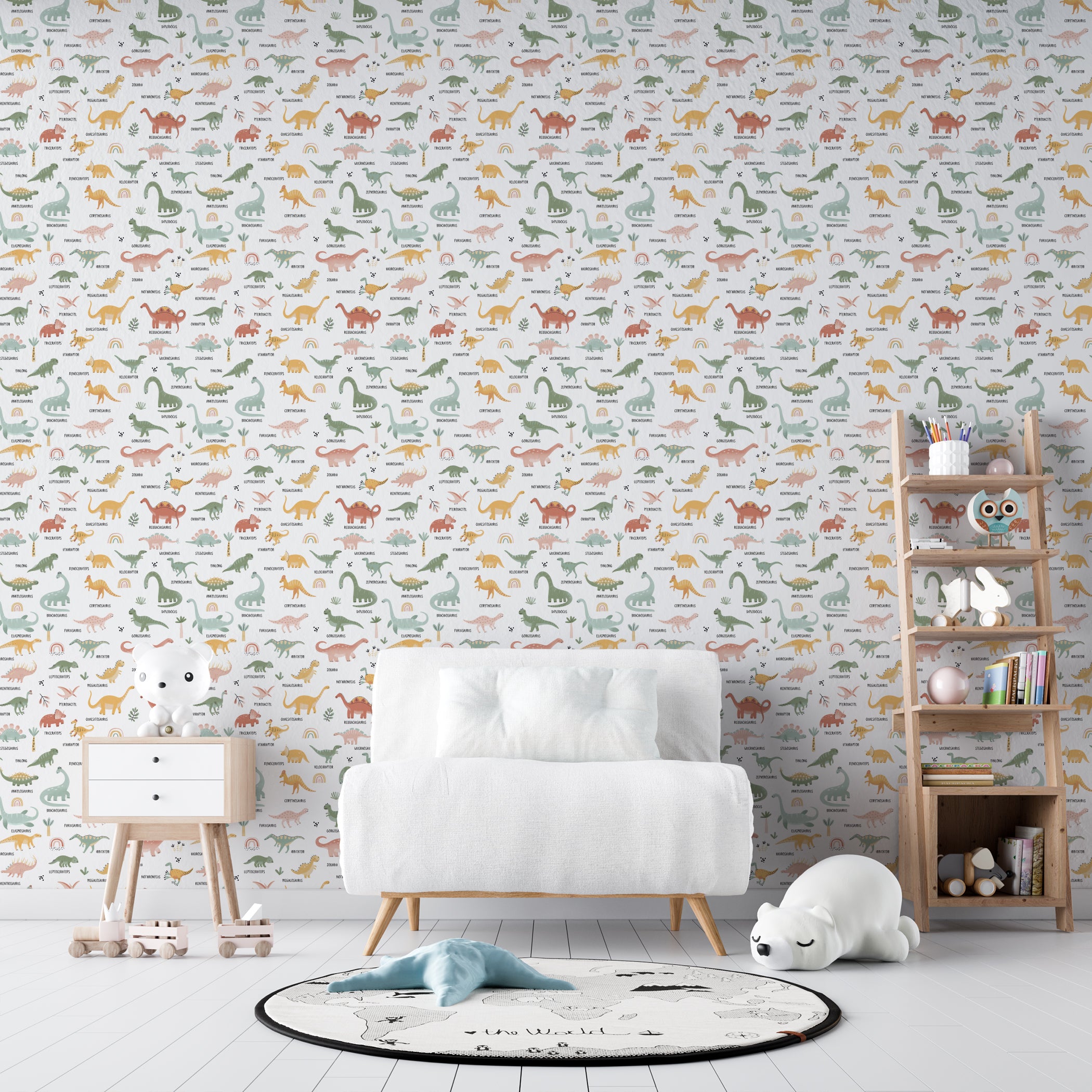 A child's room displaying the Dino World Kids Wallpaper II, which showcases a delightful array of labeled dinosaurs in muted pastels on a white backdrop adorned with green plant motifs. The setting includes a modern white chair and a wooden toy cabinet.