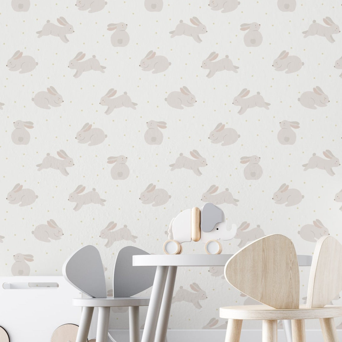 A nursery room wall covered with 'Nursery Bunny Wallpaper,' depicting adorable beige bunnies interspersed with golden dots on a light background, enhancing the tranquil and cozy ambiance of the space