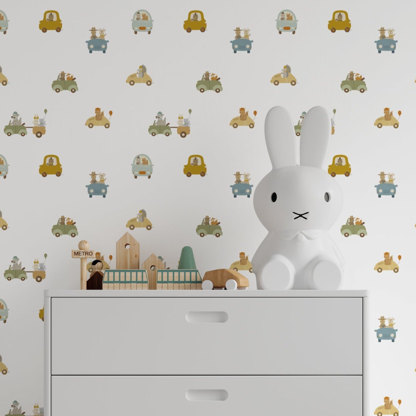 A modern child's room decorated with Road Trip Wallpaper, which displays a fun and colorful scene of animals on a road adventure, including a bunny in a white toy car on a chest of drawers, enhancing the room's playful and adventurous theme