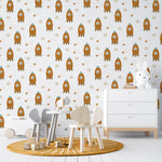 Child's playroom featuring walls adorned with Rocket Time Wallpaper, showcasing multiple orange rockets with teddy bear astronauts, interspersed with clouds and stars, complementing the playful and imaginative decor