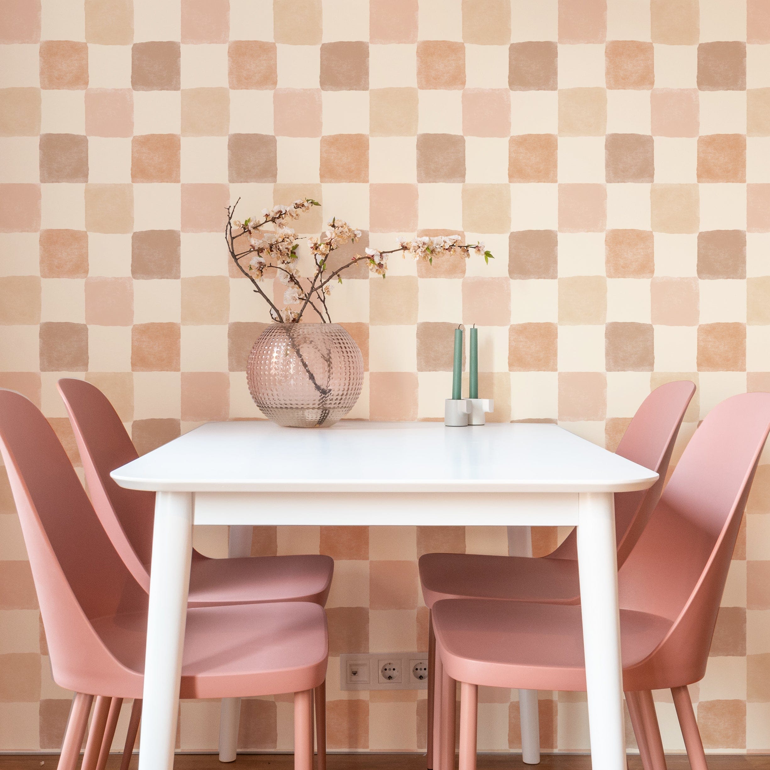 Clémence Wallpaper in a modern dining area, enhancing the space with its soothing checkered pattern of peach, taupe, and beige squares. The wallpaper pairs beautifully with pink dining chairs and a simple white table, creating a chic and cozy ambiance