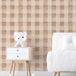 A contemporary room setting featuring Camille Wallpaper with a checkered pattern in pastel beige and cream. The room includes a modern white sofa and a wooden table with a cute white bear figurine, creating a calm and inviting atmosphere