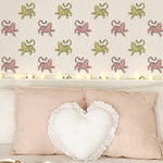 Charming children's room setup showcasing 'Cat Wallpaper 3' with leaping pink and yellow cats on the walls. The room is adorned with a heart-shaped white pillow and soft pink cushions, creating a warm and welcoming atmosphere