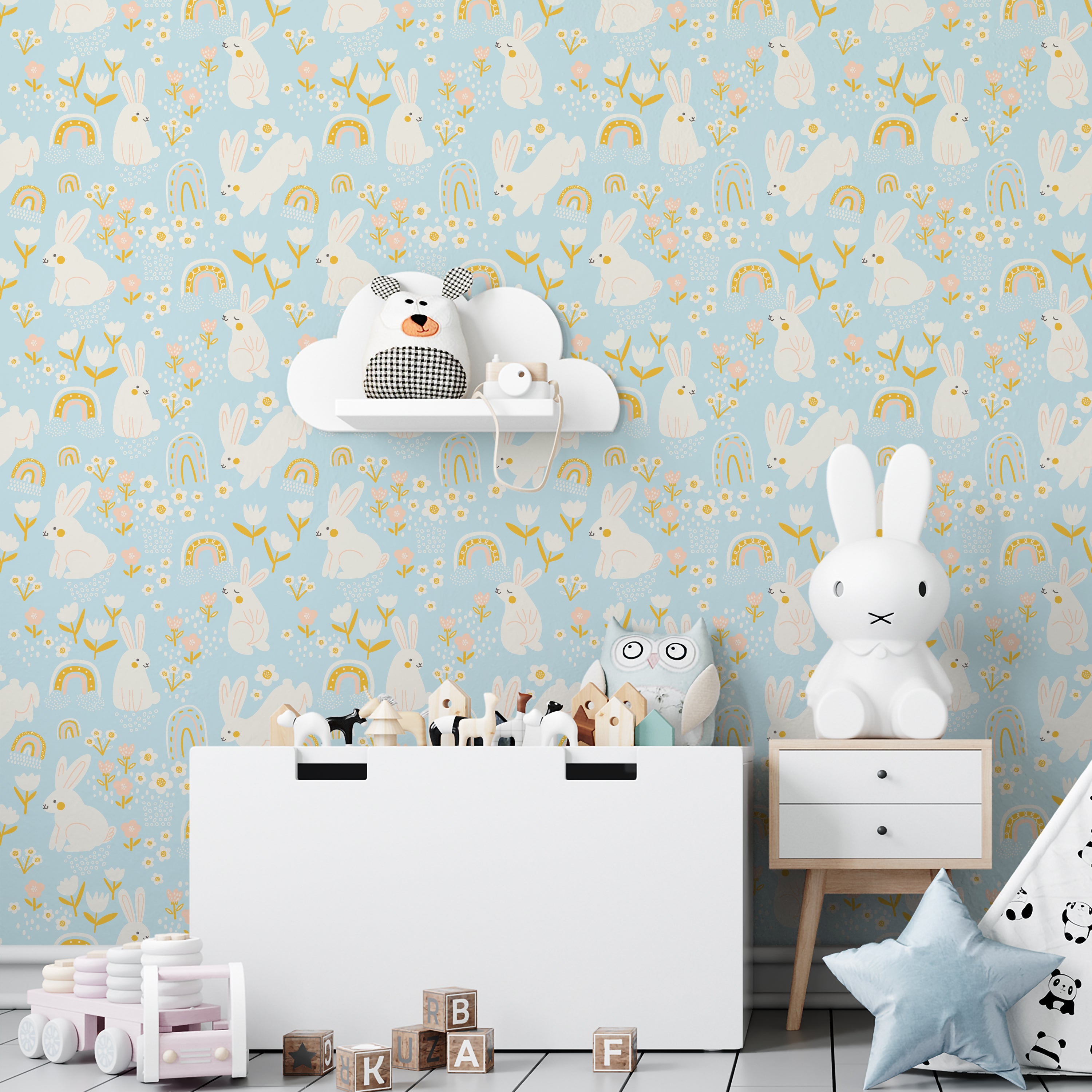 A nursery room showcasing a wall covered in light blue wallpaper featuring white rabbits and small rainbows, accompanied by child-friendly decor like toy shelves and plush animals