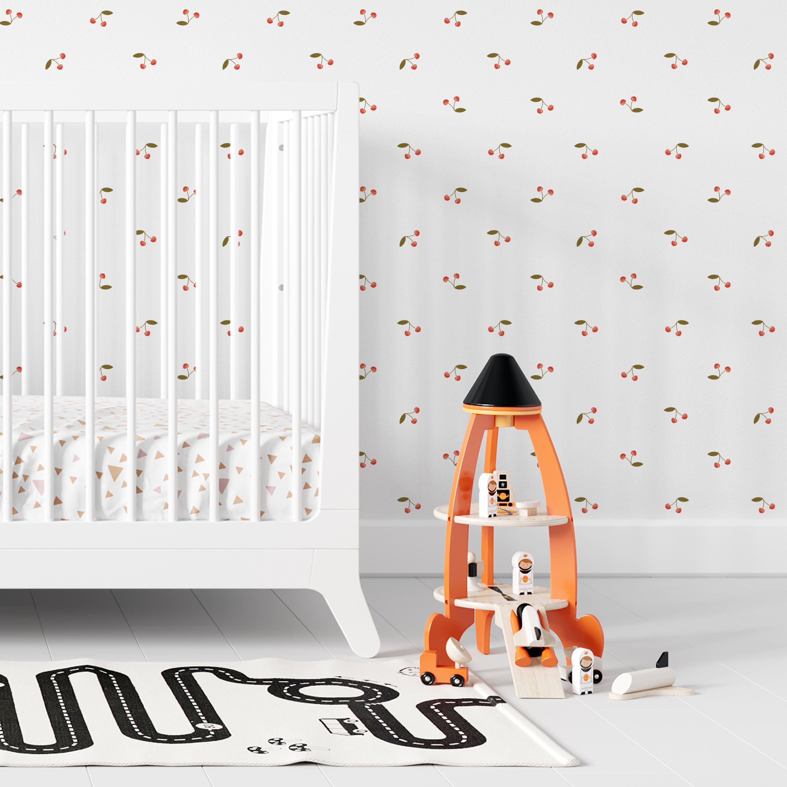 A child's nursery room wall covered with a minimalist cherry wallpaper, displaying small red cherries and green leaves on a white background, creating a playful and soothing environment