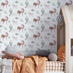 A child's bedroom wall covered with 'Watercolor Farm Animals V' wallpaper, showing pastoral scenes with horses and goats, green trees, and wooden fences, creating a tranquil farm-inspired atmosphere