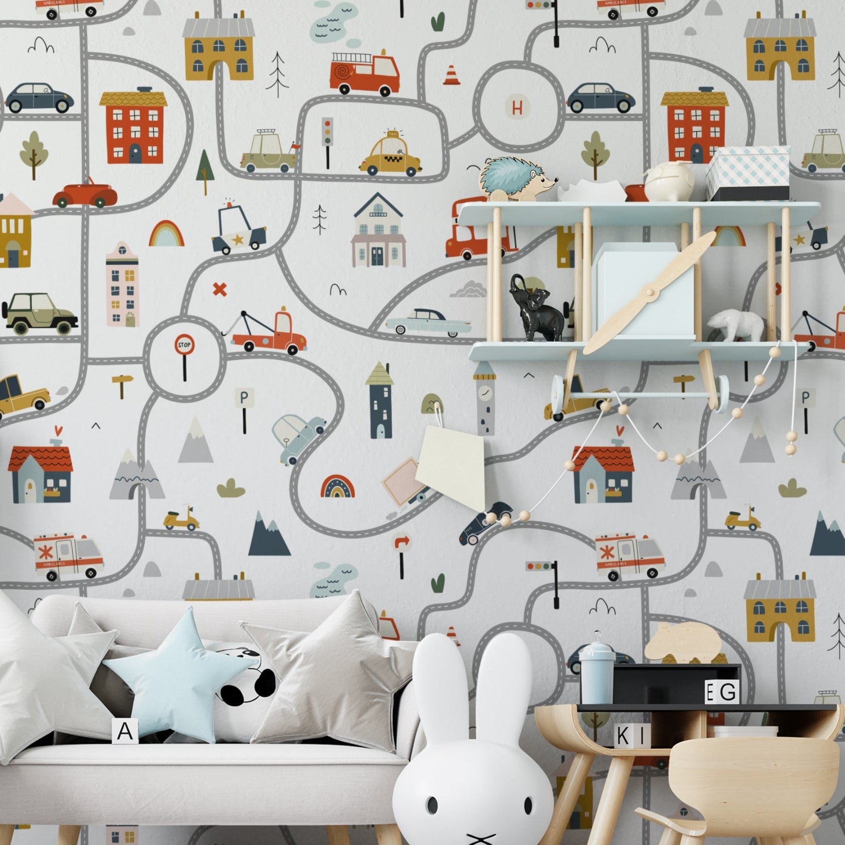 A child's bedroom wall covered with Busy Town Wallpaper, depicting a bustling town scene with whimsical roads, assorted vehicles, and charming buildings. The detailed and colorful design creates an engaging environment, complemented by children’s furniture and toys