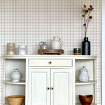 A well-arranged shelf against a backdrop of beige and white gingham wallpaper. The shelf displays various decorative items including vases, a basket, and ceramic jars, contributing to a rustic and homely aesthetic.