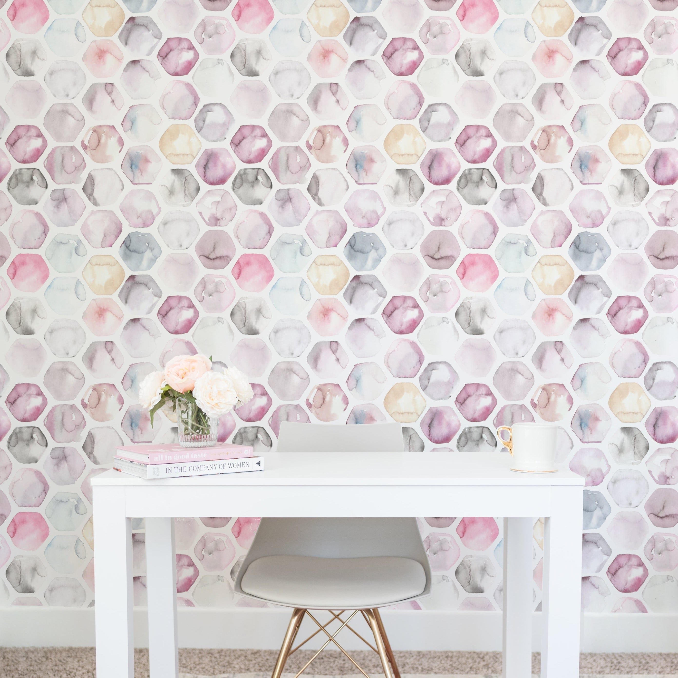 A creative workspace with the Watercolour Honeycomb Wallpaper providing an inspiring backdrop. The wall features soft, watercolor hexagons in a honeycomb pattern behind a minimalist white desk, accented by a vase of fresh flowers and simple desk accessories.