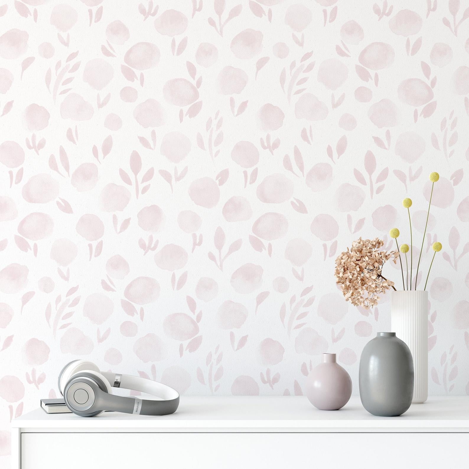 Interior setting with 'Subtle Botanica Wallpaper - II' adorning the wall, complemented by modern decor including a white vase with dried flowers, a round pink vase, and a pair of gray headphones resting on a white surface, creating a contemporary and peaceful atmosphere.
