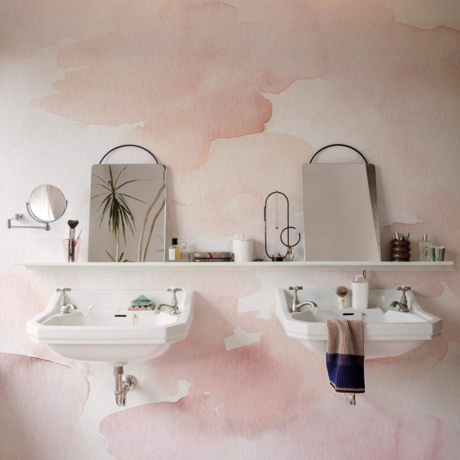 The Hand Painted Mural Wallpaper in a minimalist bathroom design, with its gentle pink watercolor strokes adding warmth and texture to the wall, harmonizing with simple white sinks and understated decor for a tranquil space.