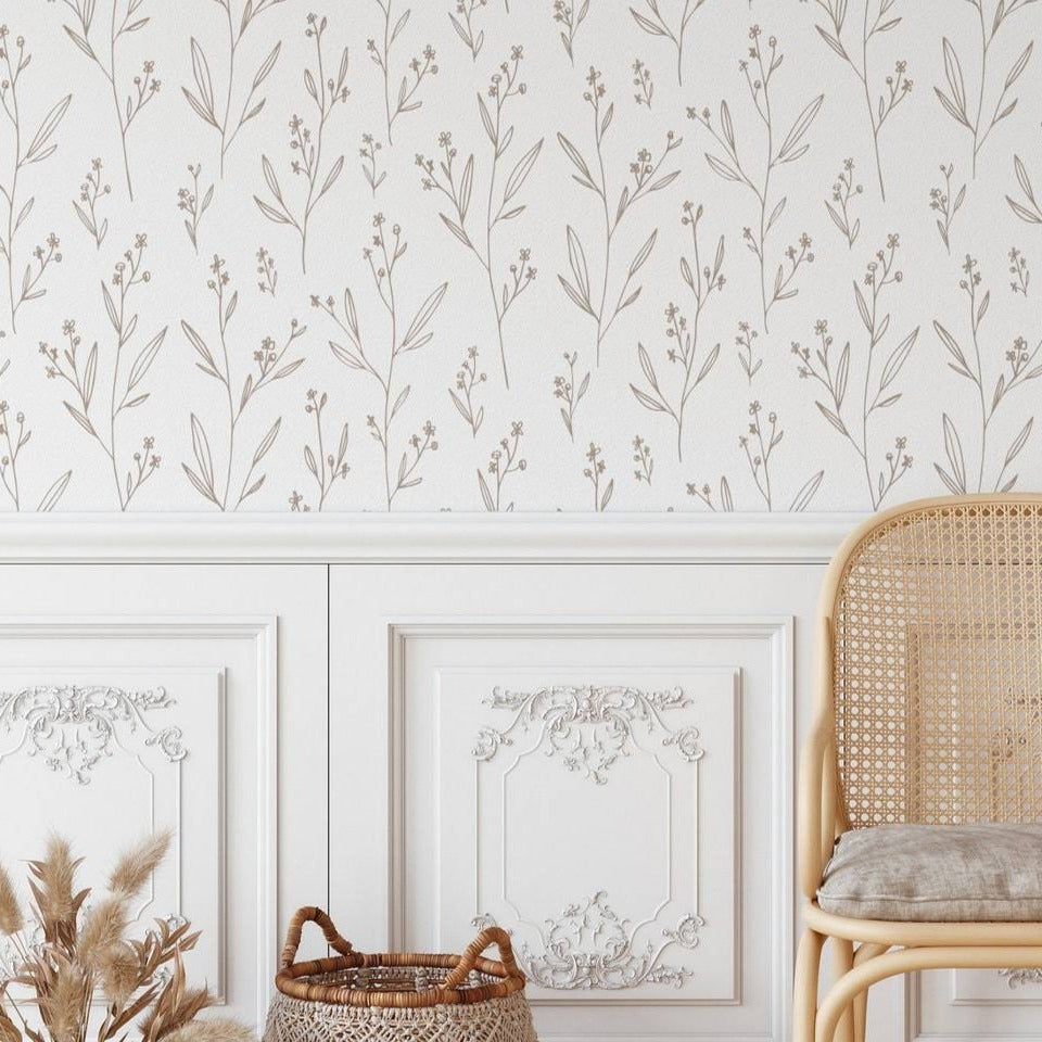 Close-up view of beige dainty minimal floral wallpaper above classic white wainscoting, paired with a cane-back chair and decorative dried pampas grass in a natural-toned basket.