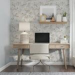 A cozy and stylish home office featuring a desk with a wooden top and golden legs, a cream upholstered chair, and a large floral wallpaper with magnolia designs adding a serene and natural touch