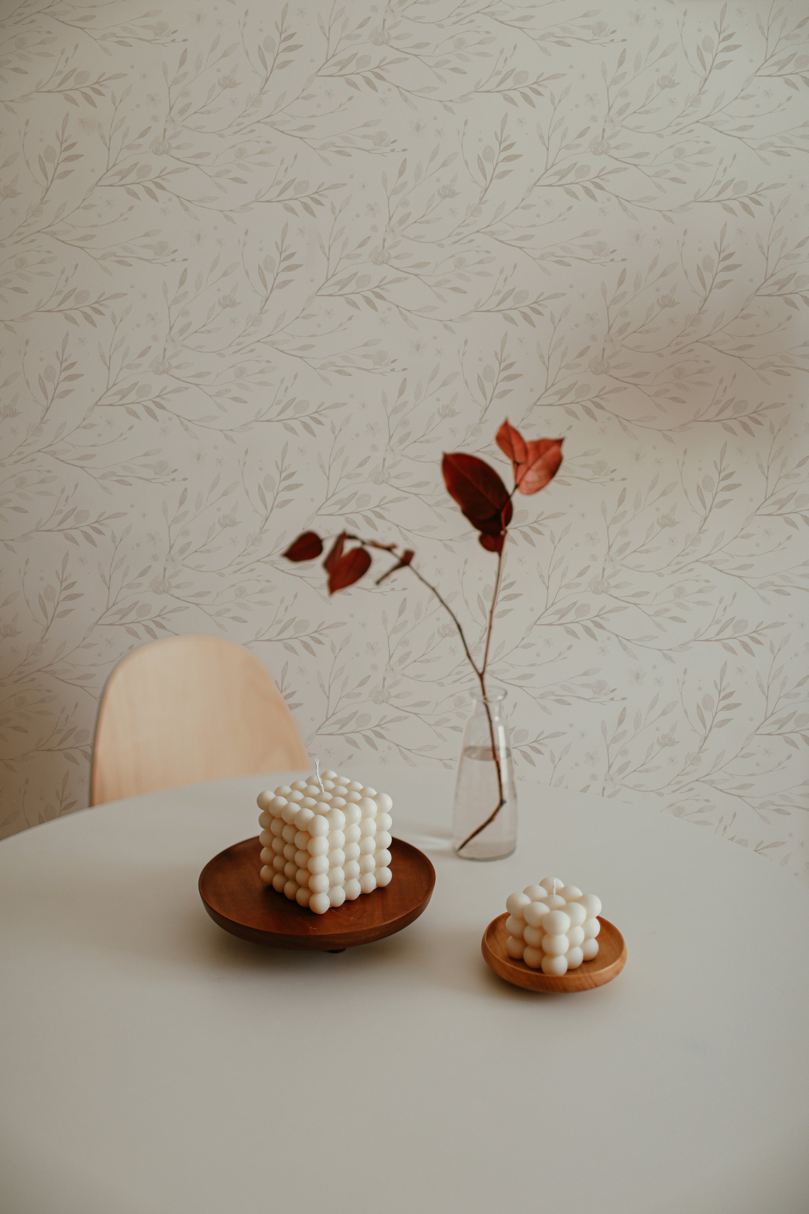 A minimalist table setting featuring a unique bubble candle against a backdrop of 'Spring Bird' wallpaper with delicate branches and leaves