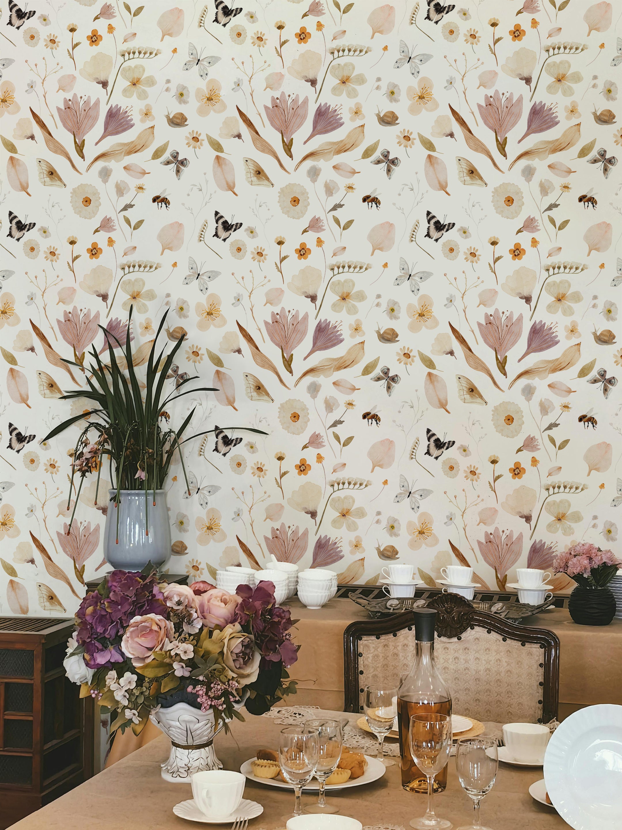 A beautifully set dining area adorned with the Boho Garden Wallpaper - 25". The wall serves as a splendid backdrop with its floral and butterfly motifs, enhancing the room's elegance and complementing the classic table setting and floral arrangements.
