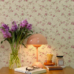 A home office setup enhanced by the Catrice Floral Wallpaper, which decorates the wall with small, detailed pink flowers and light green leaves over a faded beige background. The wallpaper pairs beautifully with contemporary room accents like a peach-colored lamp and fresh purple flowers, creating a soothing work environment.