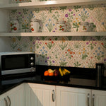 A vibrant kitchen wallpaper with a dense, colorful floral pattern featuring a variety of flowers and plants such as tulips, daisies, and bluebells. The backdrop has a warm white base with each flower meticulously illustrated in realistic colors, giving the space a lively and cheerful atmosphere.