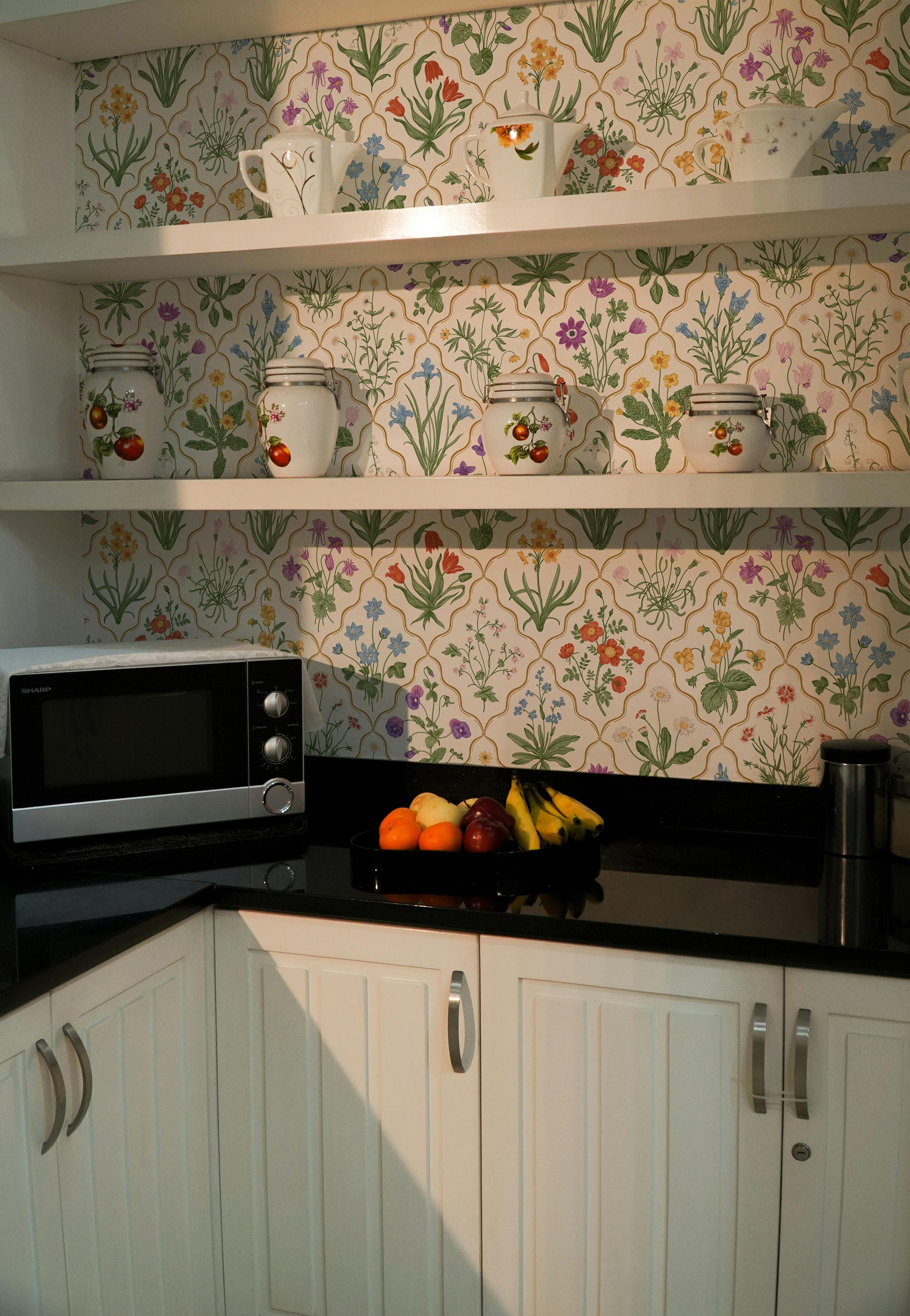 A vibrant kitchen wallpaper with a dense, colorful floral pattern featuring a variety of flowers and plants such as tulips, daisies, and bluebells. The backdrop has a warm white base with each flower meticulously illustrated in realistic colors, giving the space a lively and cheerful atmosphere.