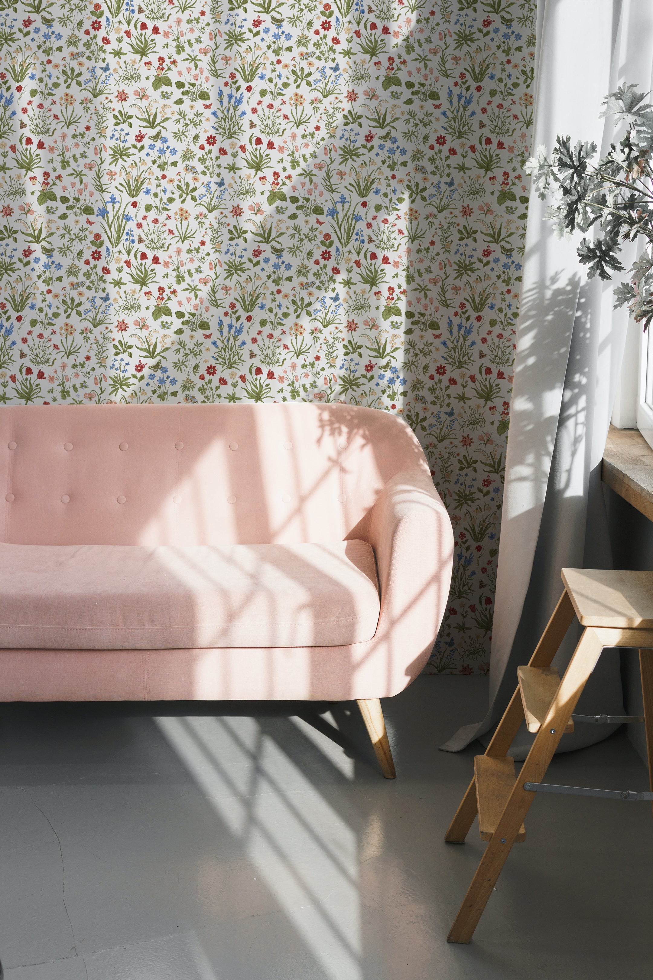 Chic living room decorated with 'Garden Fantasy Wallpaper', creating a bright and inviting space with its detailed floral print. The room is styled with a blush pink sofa and simple wooden furniture, reflecting a modern yet rustic decor style.