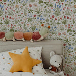 Nursery room featuring 'Garden Fantasy Wallpaper' with a diverse array of hand-drawn wildflowers in vibrant colors on a cream background, adding a joyful and colorful ambiance. A colorful caterpillar plush toy sits atop the bed, complementing the playful and nature-inspired theme of the room.