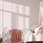 A cozy children's bedroom featuring the Daphne Floral Wallpaper with small, delicate pink floral patterns on a soft white background. The room is styled with a metal frame bed covered in pink blankets, matching pillows, and a white canopy, creating a dreamy and gentle atmosphere.