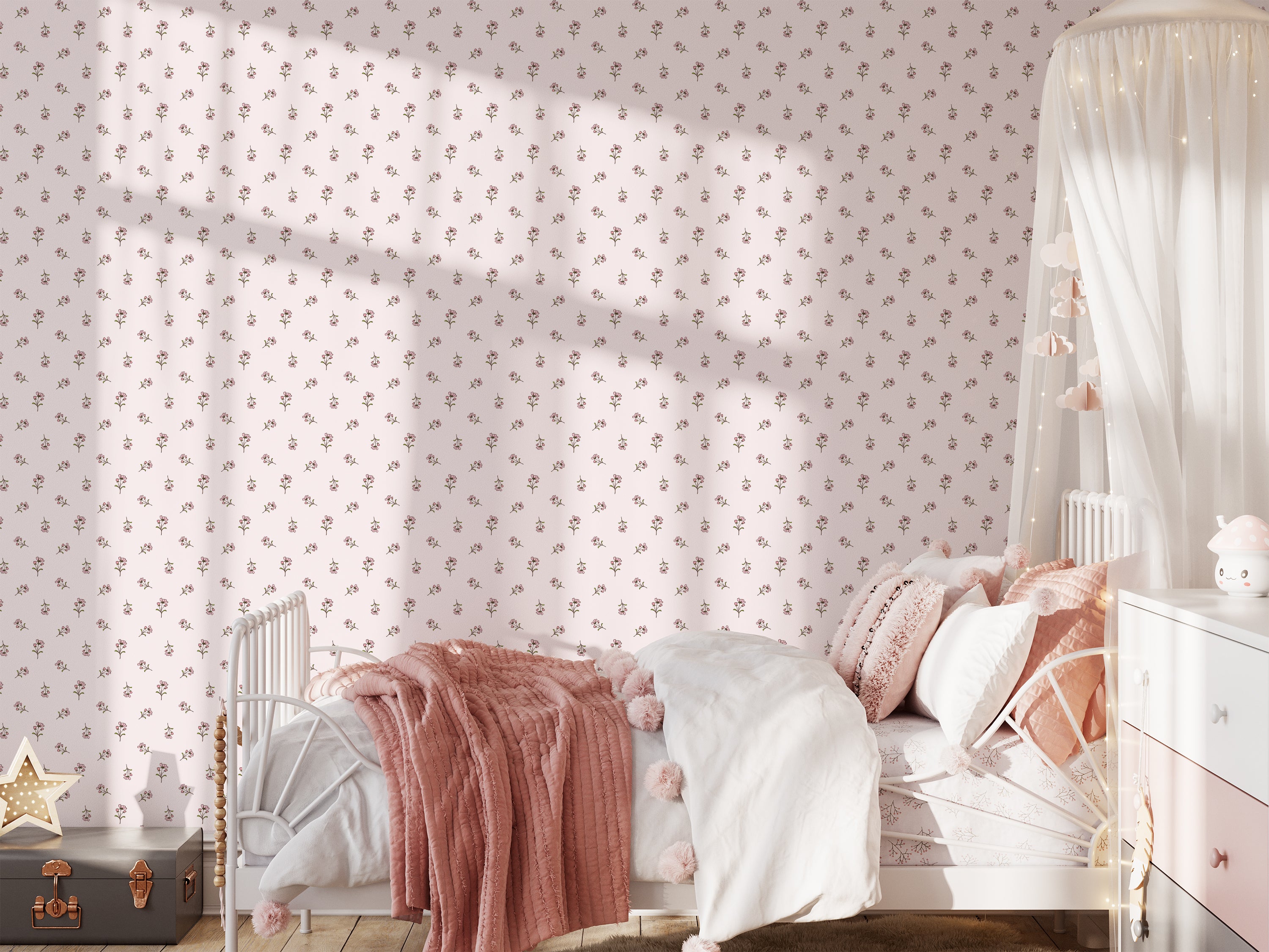 A cozy children's bedroom featuring the Daphne Floral Wallpaper with small, delicate pink floral patterns on a soft white background. The room is styled with a metal frame bed covered in pink blankets, matching pillows, and a white canopy, creating a dreamy and gentle atmosphere.