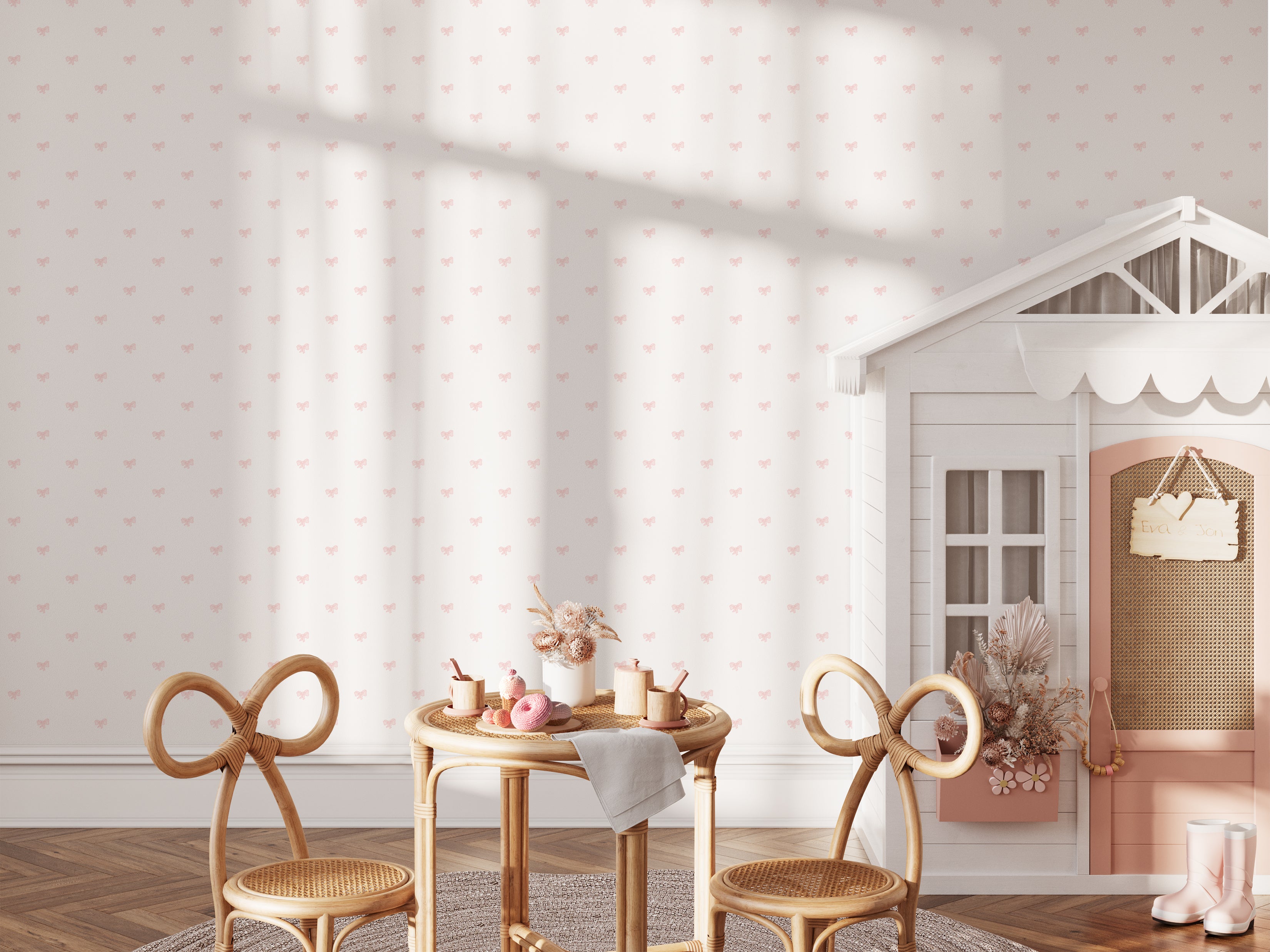 A charming child's playroom featuring the Tiny Bows Wallpaper, adorned with small pink bows on a light cream background. The room includes a playful house-shaped bookcase, a rattan children's table set, and a decorative floor rug.