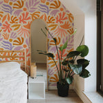 Cozy room corner showcasing an arch-shaped mirror and a large potted plant in front of a lively wallpaper with an abstract plant motif in warm tones