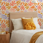 Contemporary bedroom with a headboard against a vibrant wallpaper featuring abstract botanical shapes in orange, purple, and yellow hues.