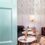 Chic café interior with turquoise door, featuring walls adorned with a fish pattern wallpaper in a delicate teal shade above white wainscoting
